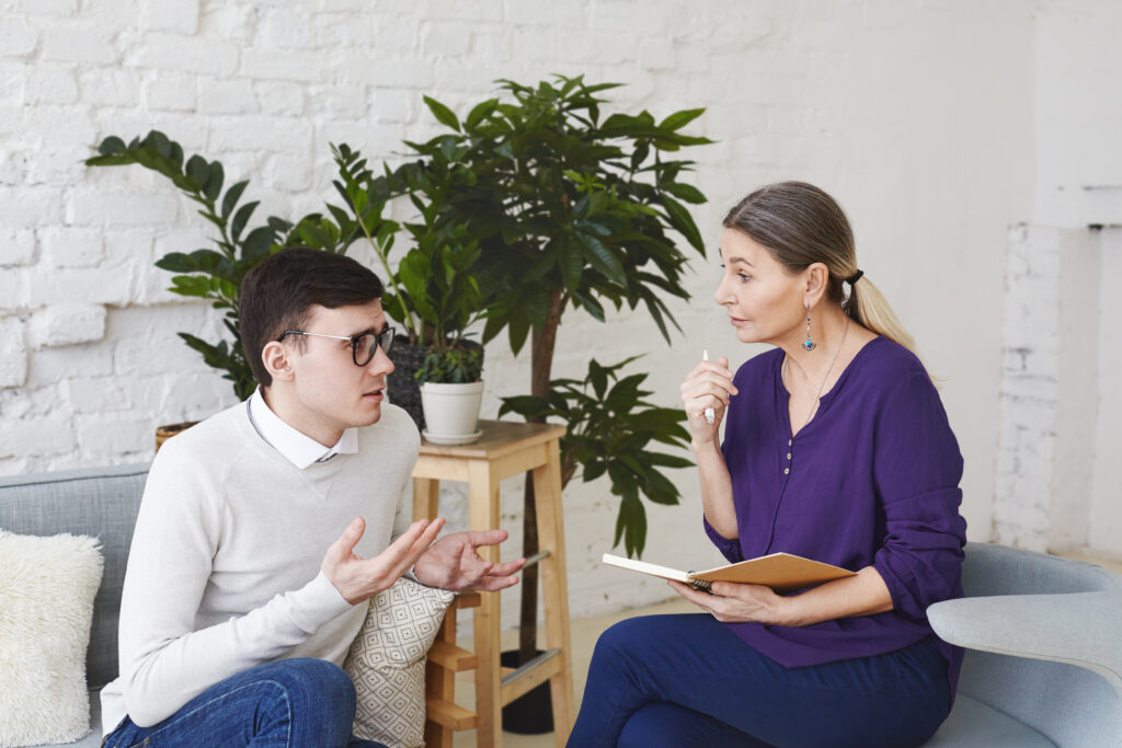 Young man talking to therapist in welcoming environment, representing emotional support for students.
