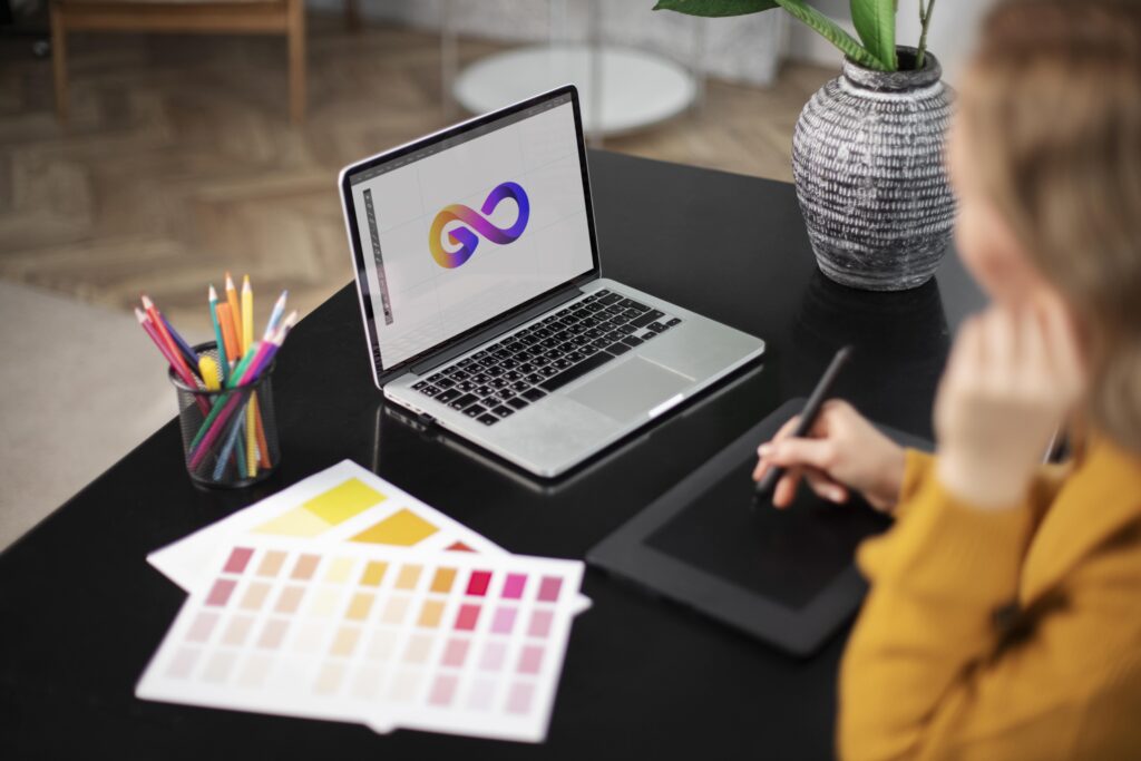 Student working on a graphic design project with a graphics tablet and laptop, surrounded by color palettes and colored pencils.