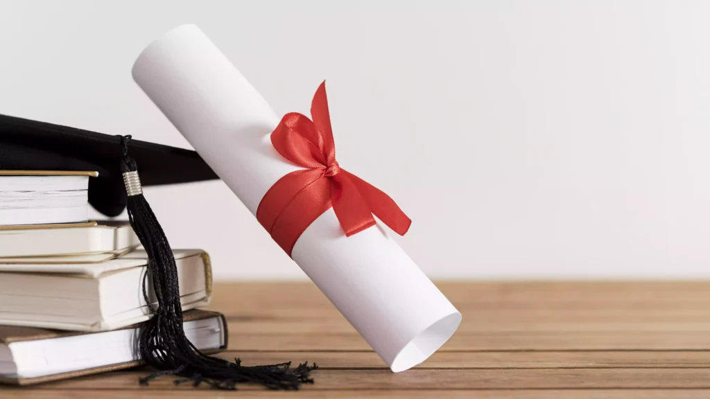 Diploma enrolado com laço vermelho sobre pilha de livros e capelo de formatura, simbolizando a conquista de um Diploma Canadense.