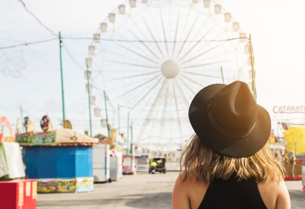 Young man in black hat watching Ferris wheel at an outdoor cultural event in Canada, representing participation in local festivals and celebrations.