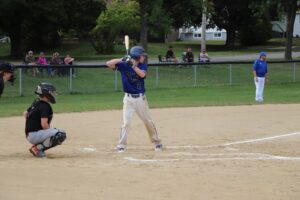 Estudiante con uniforme azul sosteniendo un bate de béisbol en el campo, listo para batear, representando las Materias Optativas.