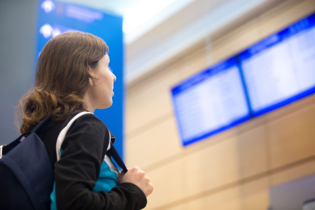 Jovem com mochila olhando painel de voos em aeroporto, representando o serviço de recepção no aeroporto para estudantes internacionais no Canadá.