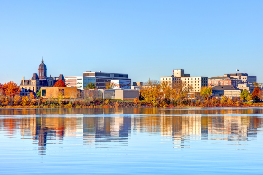 View of the city of Saint Andrews, Canada, with historic buildings and trees in autumn tones reflected in the river.