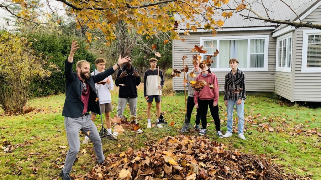 Grupo de estudantes com supervisor ao ar livre, participando de atividade com folhas de outono, simbolizando segurança, integração e bem-estar na Fredericton Christian Academy.