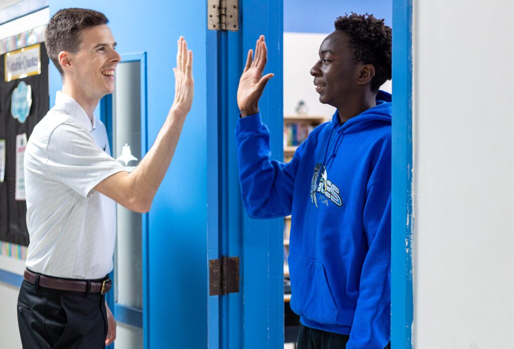 Professor cumprimentando aluno da Fredericton Christian Academy no corredor da escola, representando o acompanhamento acadêmico próximo e individualizado.