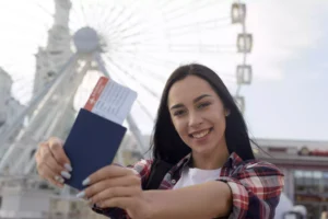 Estudiante sonriente con pasaporte y billete de avión delante de la noria, que simboliza un viaje de intercambio a Canadá.