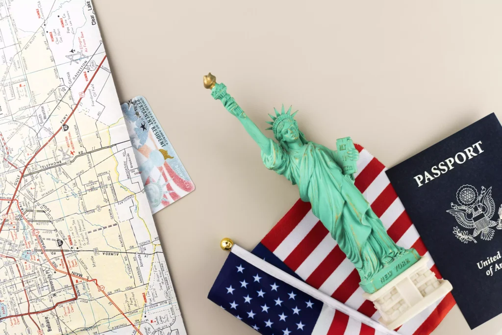 United States passport next to Statue of Liberty, American flag, map and permanent residence card.