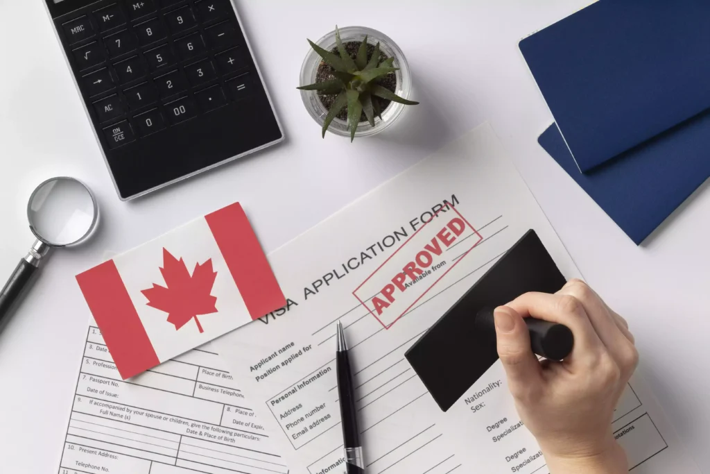 Formulario de solicitud de visa canadiense aprobado con sello, junto a pasaportes, bandera canadiense y calculadora.