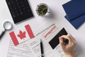 Formulario de solicitud de visa canadiense aprobado con sello, junto a pasaportes, bandera canadiense y calculadora.
