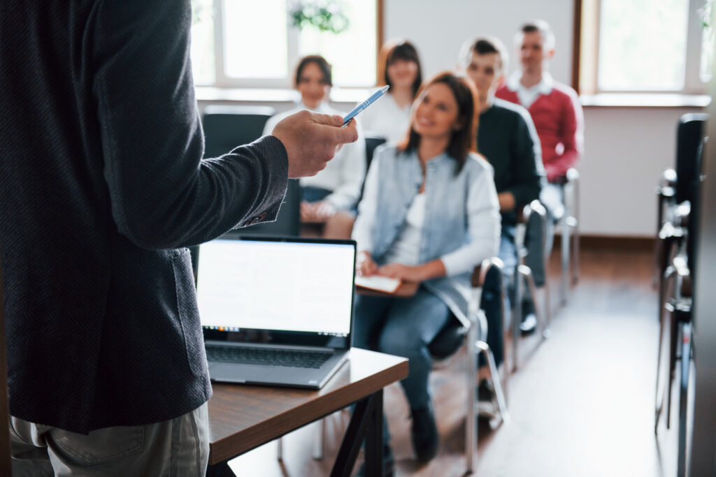 Profesor dirigiendo una clase con un grupo de estudiantes universitarios atentos y sonrientes en un aula moderna.