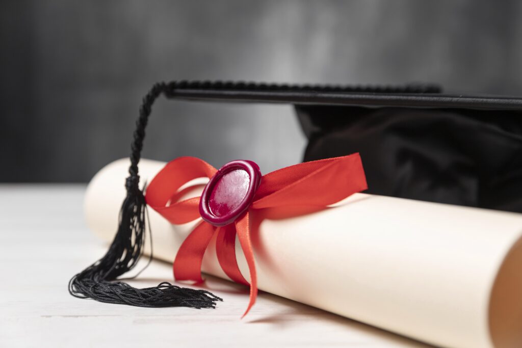 Diploma de licenciatura con sello de cera roja y birrete de graduación negro sobre una mesa de luz.