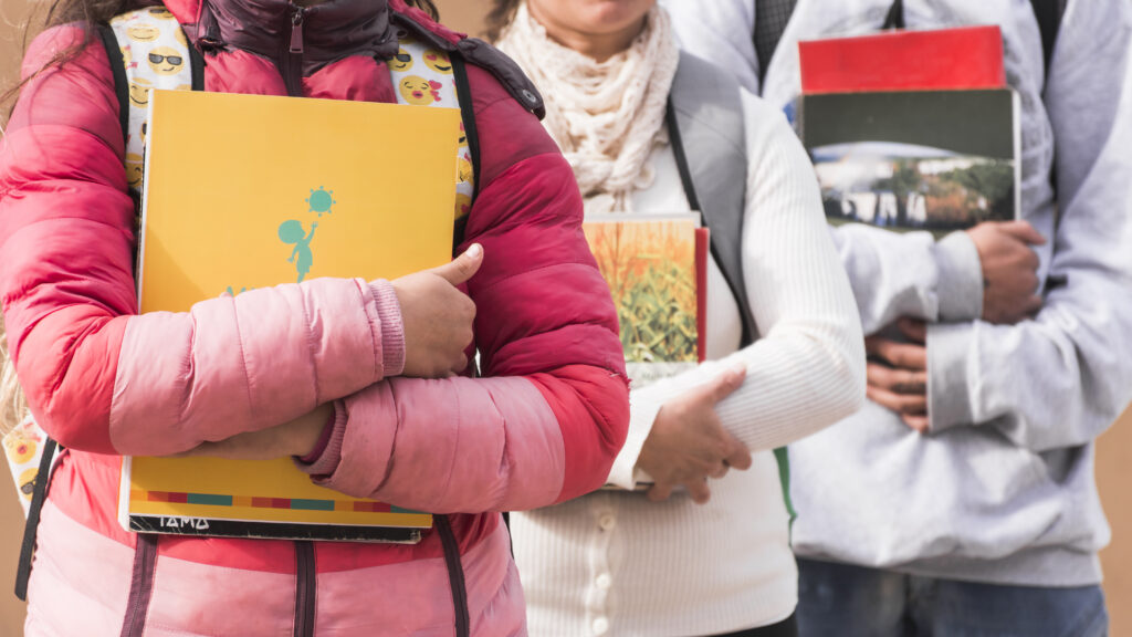 Estudiantes sosteniendo libros y cuadernos cerca del cuerpo